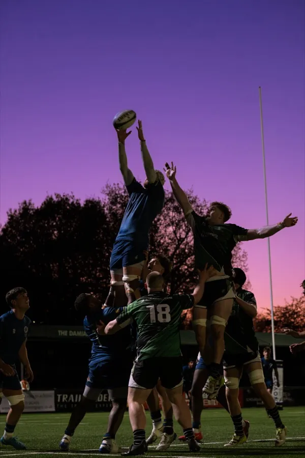 A Brunel lineout jumper is lifted above the opposition to take the ball against a purple dusk sky.