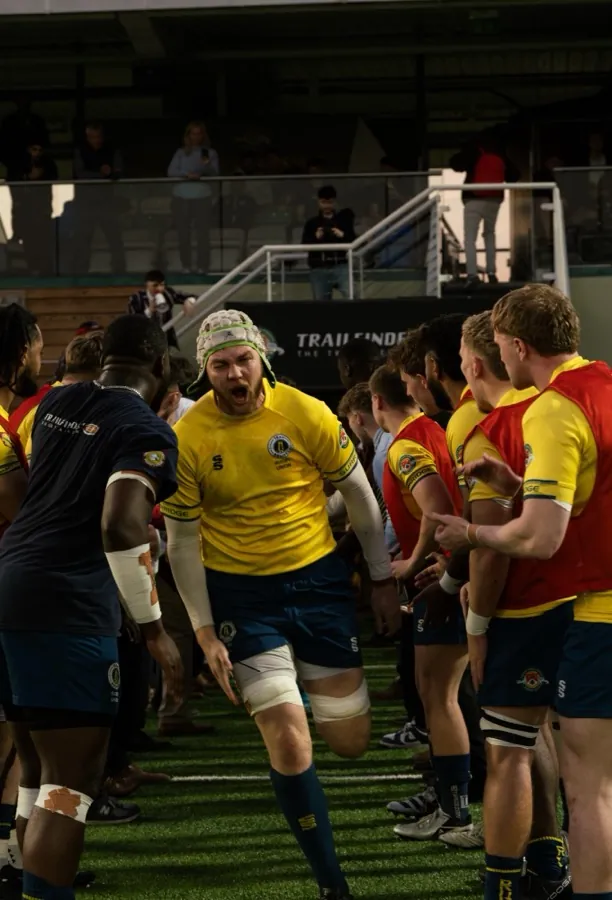 A Brunel player in the gold shirt roars as he runs out between two lines of team-mates.